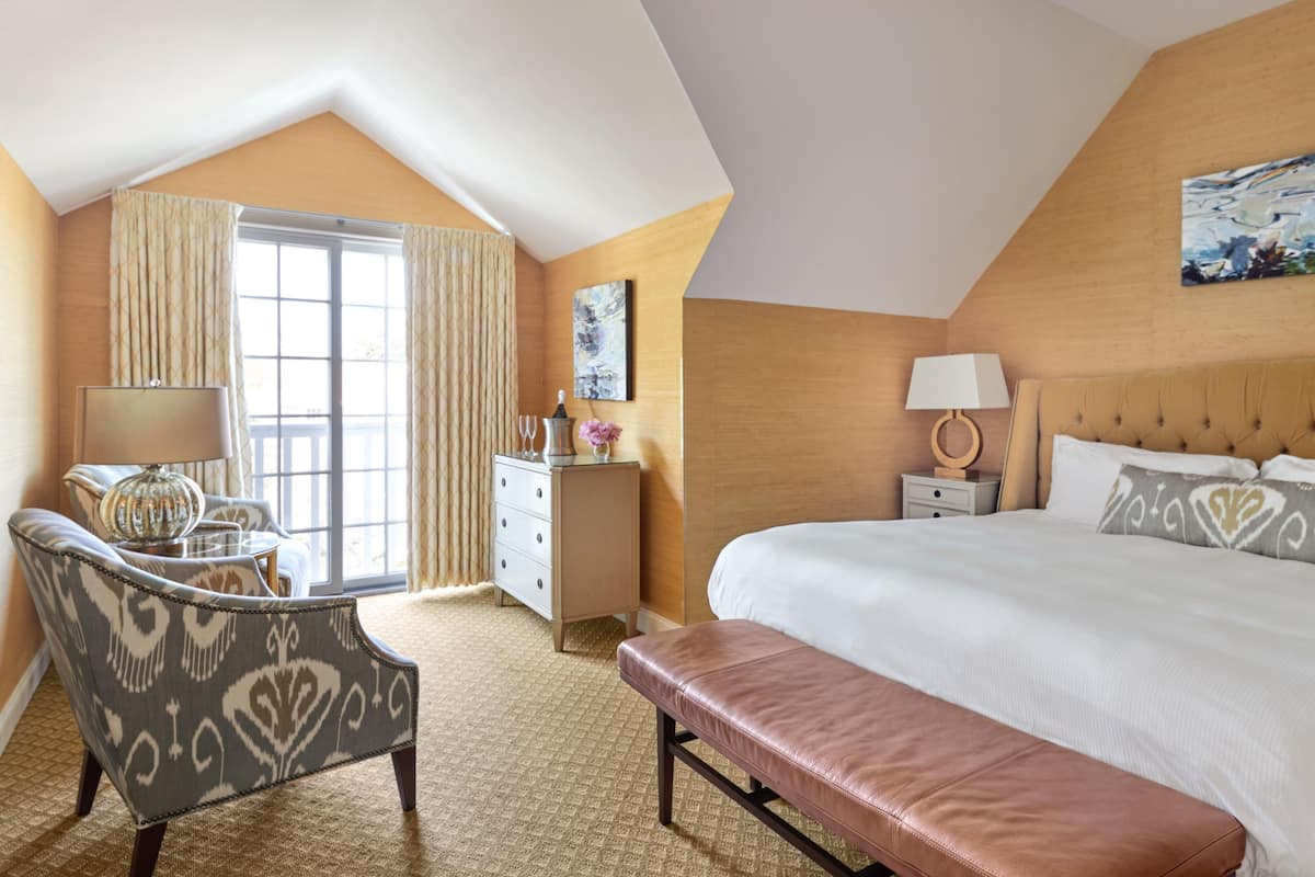 A hotel room with a large bed, a desk, a chair, a bench, a dresser, and a window with curtains.