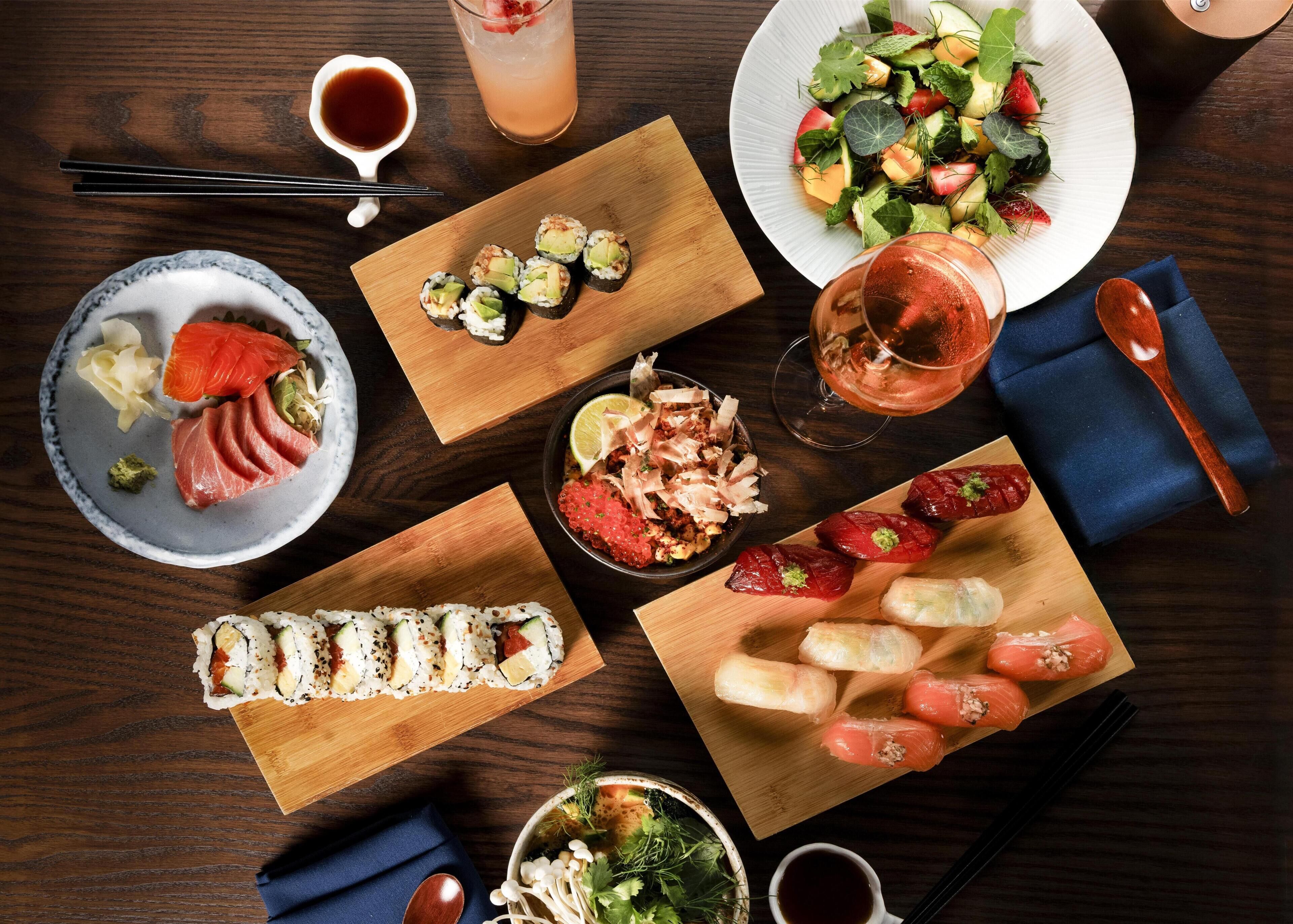 A variety of sushi and sashimi dishes on wooden boards, a salad plate, and a bowl of pickled vegetables.