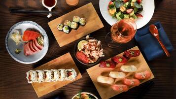 A variety of sushi and sashimi dishes on wooden boards, a salad plate, and a bowl of pickled vegetables.