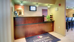 Un'area reception di un hotel con una scrivania in legno, uno schermo digitale che mostra informazioni dell'hotel e un tappetino d'ingresso con il nome dell'hotel.