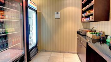 Una kitchenette con un refrigerador lleno de bebidas, un microondas y una alacena con aperitivos.