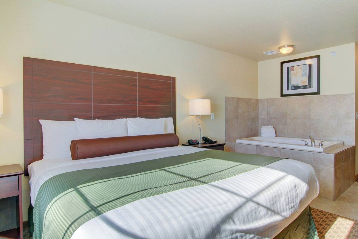 Ein Hotelzimmer mit einem großen Bett, einem Badezimmer mit einer Badewanne und einem gerahmten Bild an der Wand.
