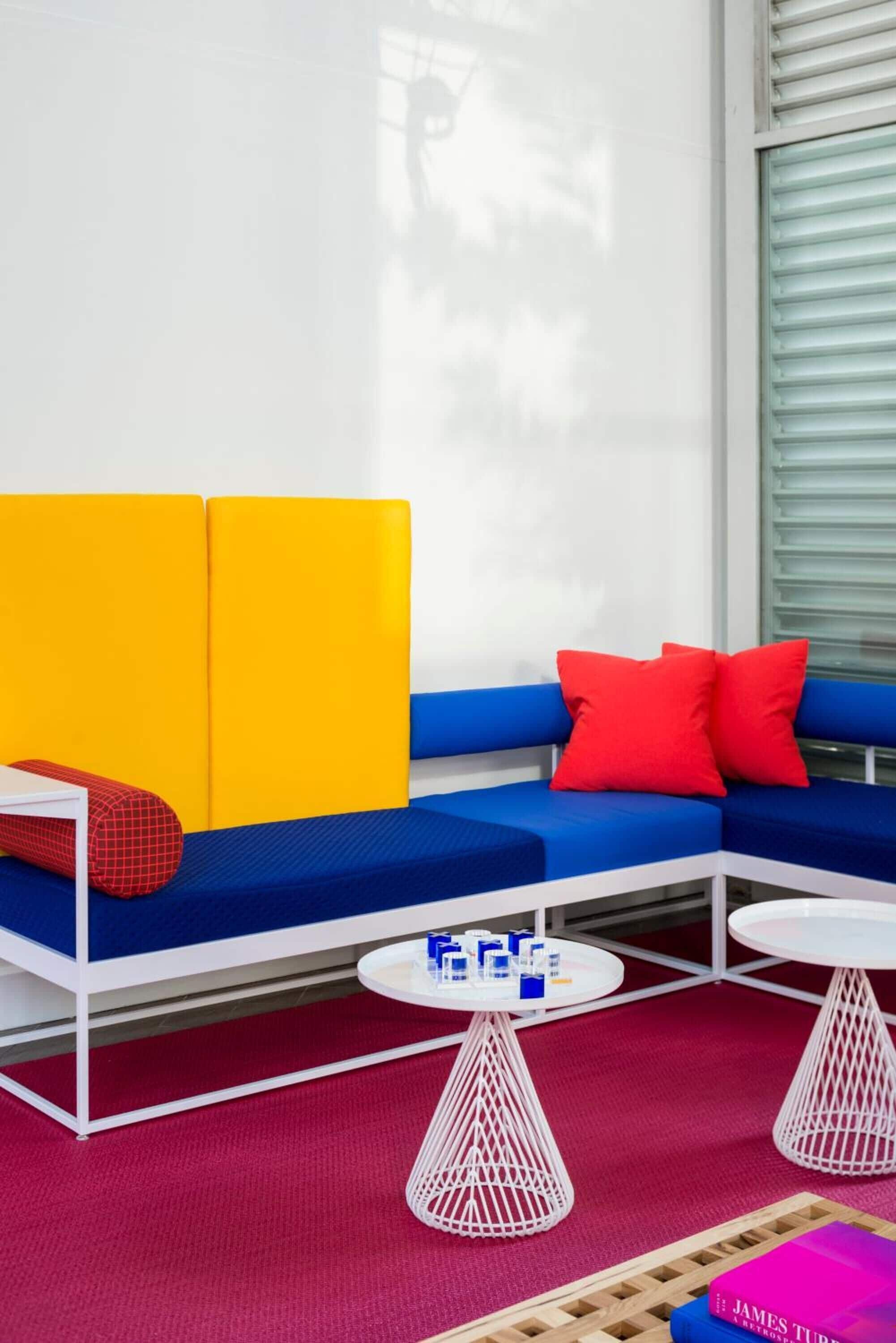 A modern room with a blue sofa, red pillows, and two white tables with a red carpet.