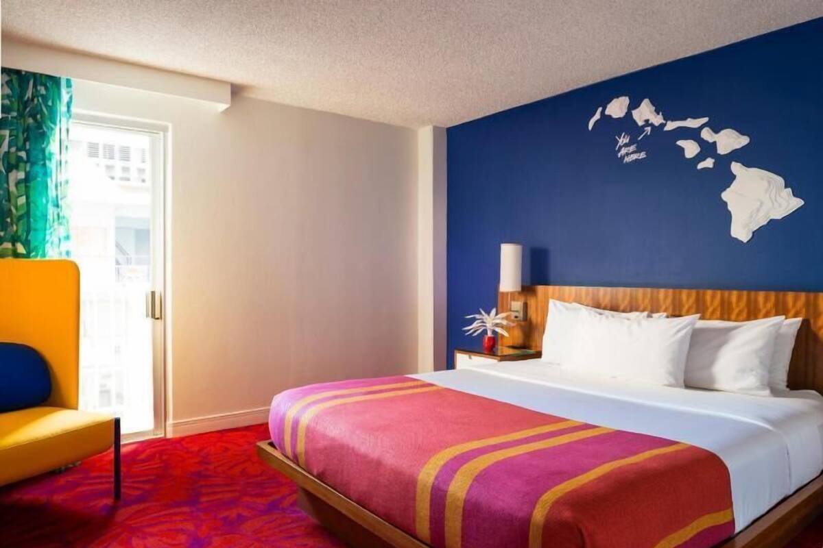 A hotel room with a bed, a nightstand, a lamp, a chair, and a wall map.
