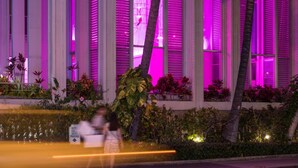 Um edifício com colunas verticais e varandas, iluminado por luzes cor de rosa.