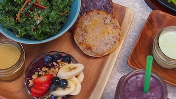 A breakfast tray with a bowl of kale salad, a slice of toast, a bowl of granola with fruit, and a glass of smoothie.