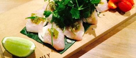 A wooden serving board with sliced fish, garnishes, and a lime wedge.