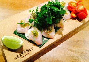 Una tabla de madera con pescado en rodajas, guarniciones y un gajo de lima.