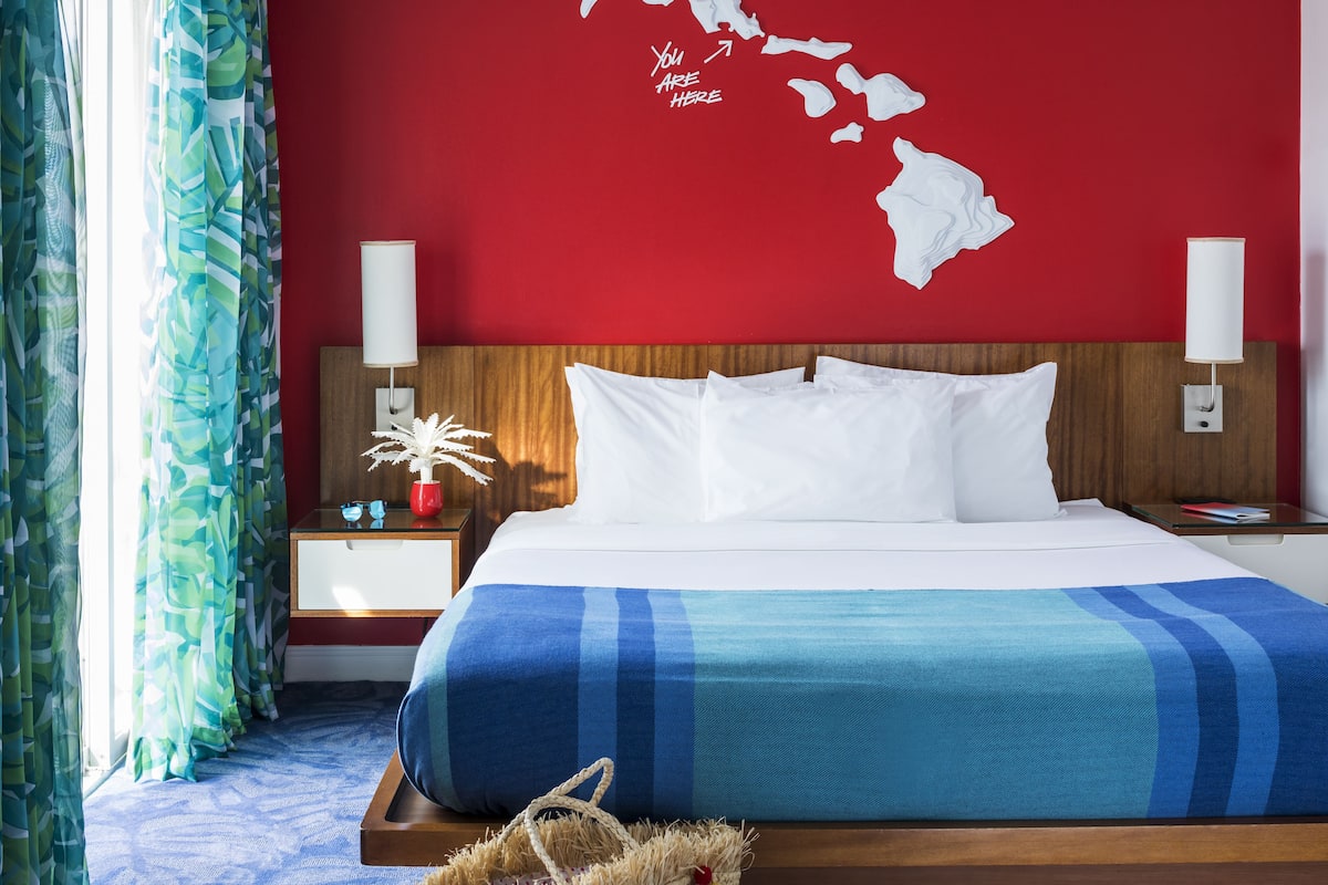 A hotel room with a bed, a map on the wall, a nightstand, and a window with curtains.
