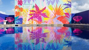 Une fresque colorée aux motifs tropicaux se reflétant dans une piscine.