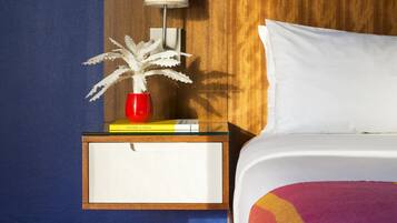 A hotel room with a bed, a nightstand with a lamp, a red vase, and a book.