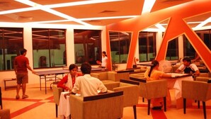 A modern lounge area with tables and chairs, large windows, and a distinctive orange architectural design. - Country Spa Wellness Beach Resort (Thiruvananthapuram)