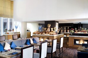 A modern restaurant with a central bar area, seating with blue cushions, and a variety of food and drink displays.