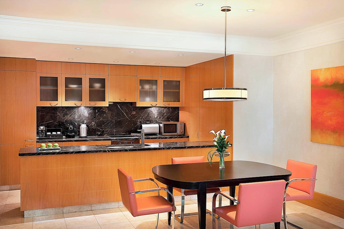 A modern kitchen with wooden cabinets, a black countertop, and a dining area with a table and chairs.