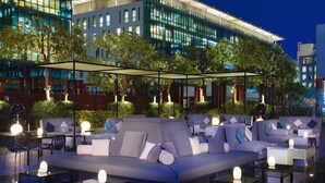 Un espace extérieur aménagé avec des canapés et des tables, une partie abritée et un bâtiment moderne en arrière-plan.