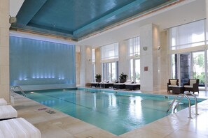 An indoor swimming pool with clear water, lounge chairs, and a blue ceiling.