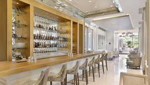 Un espace bar moderne doté d’un long comptoir, de nombreux tabourets et d’étagères remplies de bouteilles et de verres.