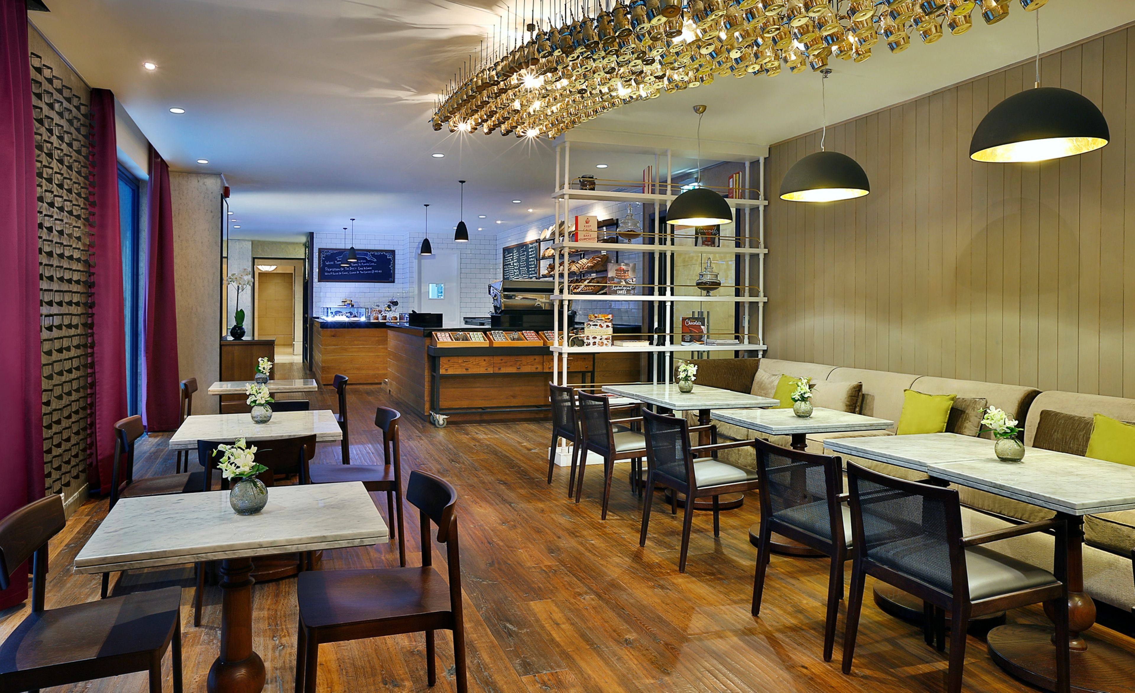 Un interior de restaurante con suelo de madera, mesas, sillas, una zona de bar y un candelabro colgante.