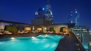 Une piscine sur le toit, dotée de chaises longues et offrant une vue sur les gratte-ciel de la ville la nuit.