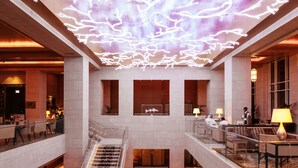 Un hall d’hôtel à plusieurs niveaux, doté d’un design moderne, comprenant un escalier central, des espaces de détente et un plafond avec un système de projection lumineuse.
