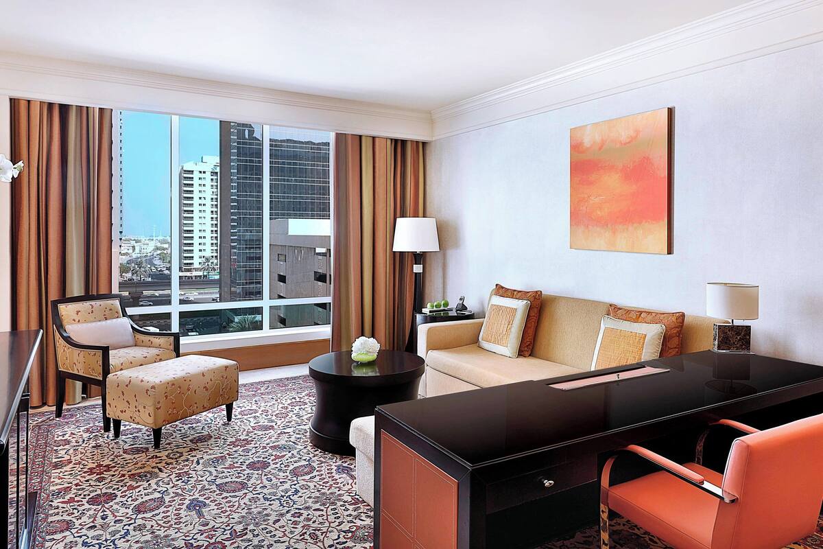 A hotel room with a large window, a sofa, a desk, and a chair.