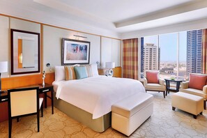 A hotel room with a large bed, a desk, a chair, a sofa, and a view of the city.