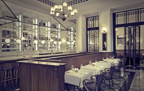 Restaurante com um balcão comprido, várias mesas e um espaço de bar com prateleiras cheias de garrafas e copos.
