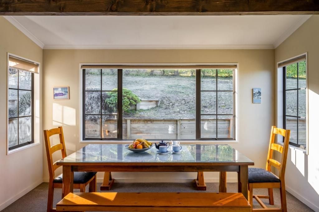 A dining area with a glass table, chairs, and a view of a garden through large windows.