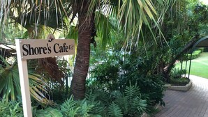 A sign for 'Shore's Cafe' amidst lush greenery and a paved walkway.
