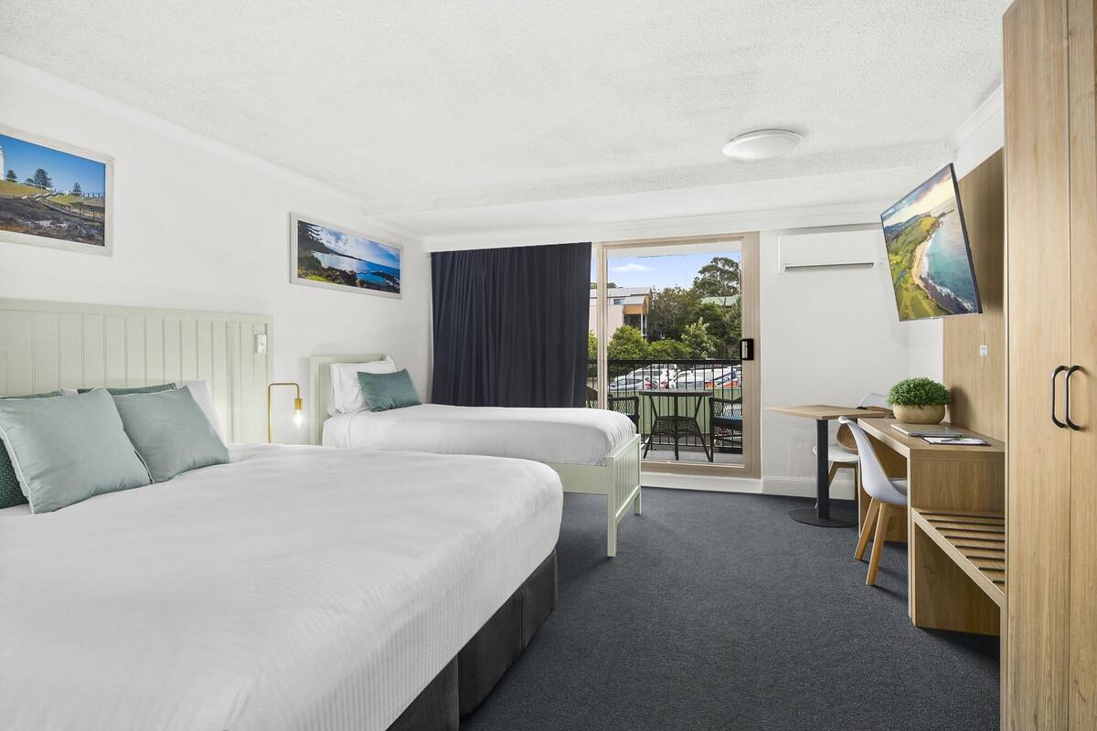 Une chambre d’hôtel avec deux lits, un bureau, une chaise, une petite table et un balcon avec vue.