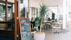 An outdoor seating area with a chalkboard menu, wooden chairs, and a large potted plant.