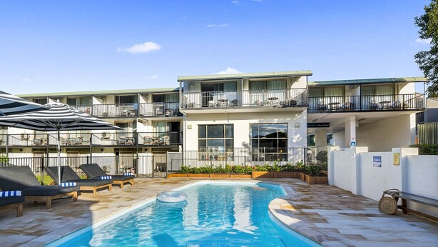 A poolside area with a swimming pool, lounge chairs, and a building with multiple balconies.