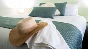 A neatly made bed with green and white bedding, a straw hat, and a white towel.