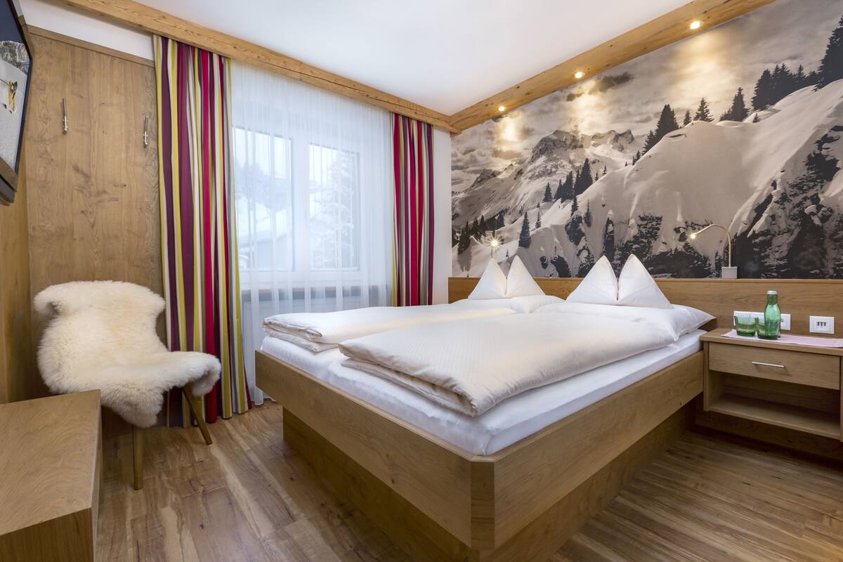 A bedroom with a wooden bed, a fluffy chair, a nightstand, and a mountain mural on the wall.