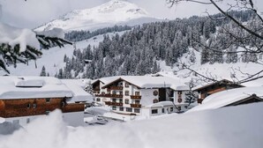 A snow-covered mountain resort with chalet-style buildings, ski lifts, and dense forested slopes. - Hotel Garni Lavendel (Lech am Arlberg)