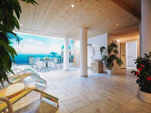 A spacious indoor area with a tiled floor, a balcony with a view of the sea, and a seating area with a table and chairs. - Hotel Garni Lavendel (Lech am Arlberg)