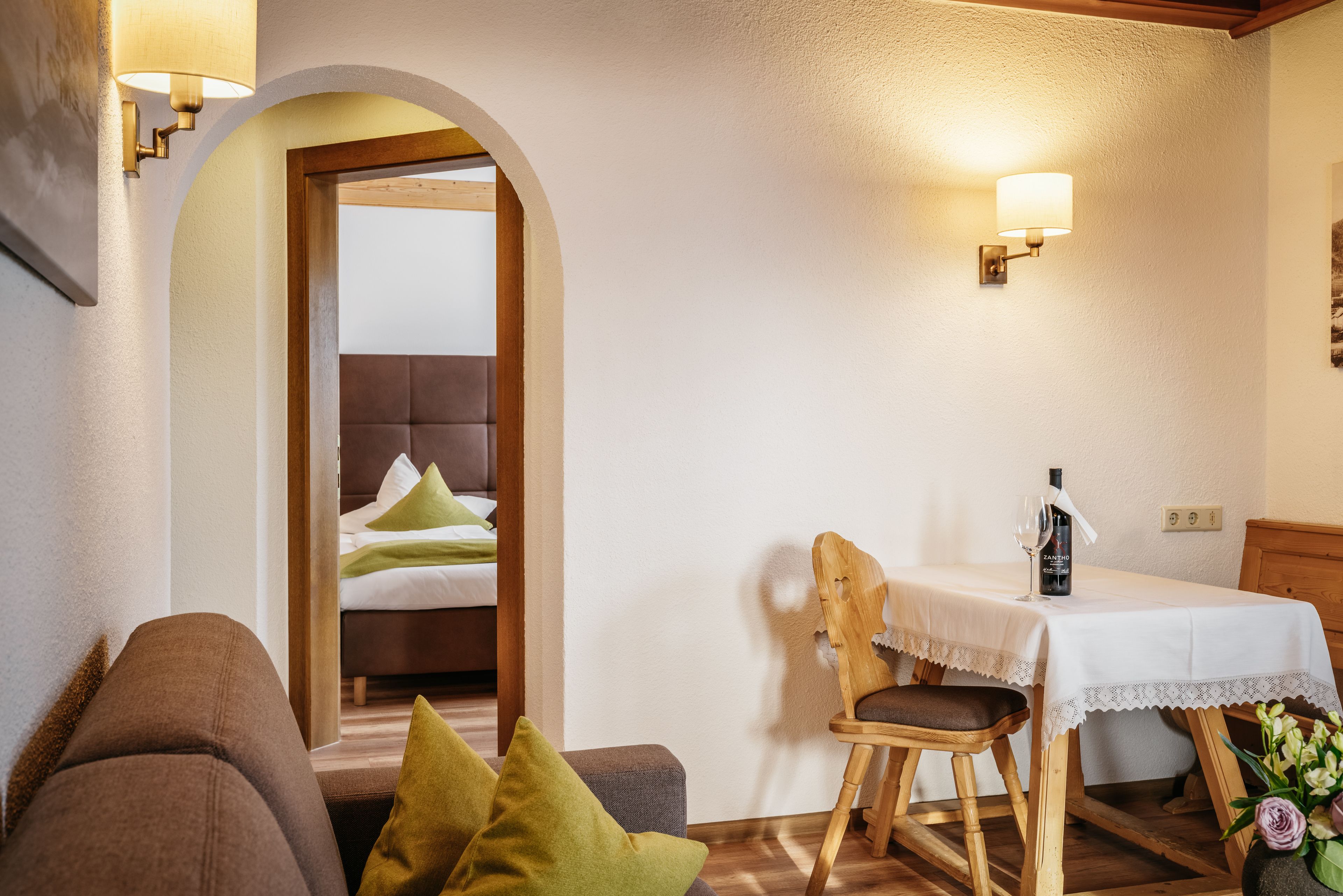 Una habitación acogedora con una mesa de madera, una silla con cojín y un sofá.