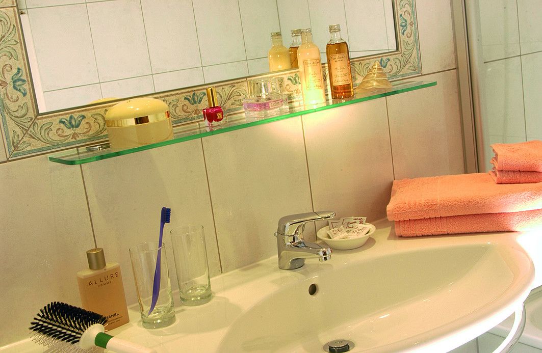 A bathroom with a white sink, a glass shelf with toiletries, a toothbrush, and a towel.