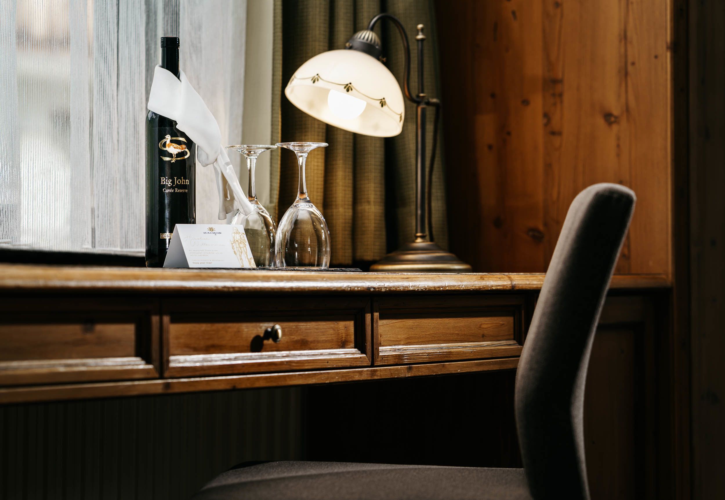 A wooden desk with a bottle of wine, glasses, and a lamp.