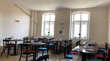 A dining area with multiple tables and chairs, large windows, and a wall-mounted light fixture.