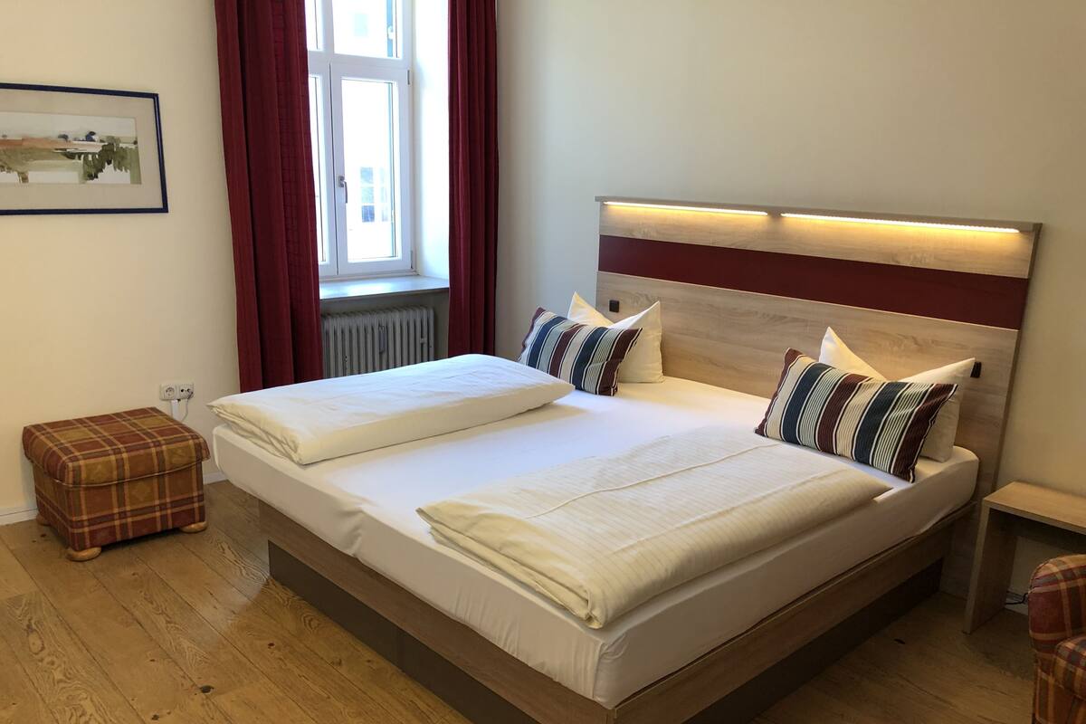 Ein Doppelbett mit Holz-Kopfteil, zwei Nachttische und ein karierter Hocker.