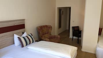 A hotel room with a bed, a plaid armchair, a black chair, and a wooden floor.