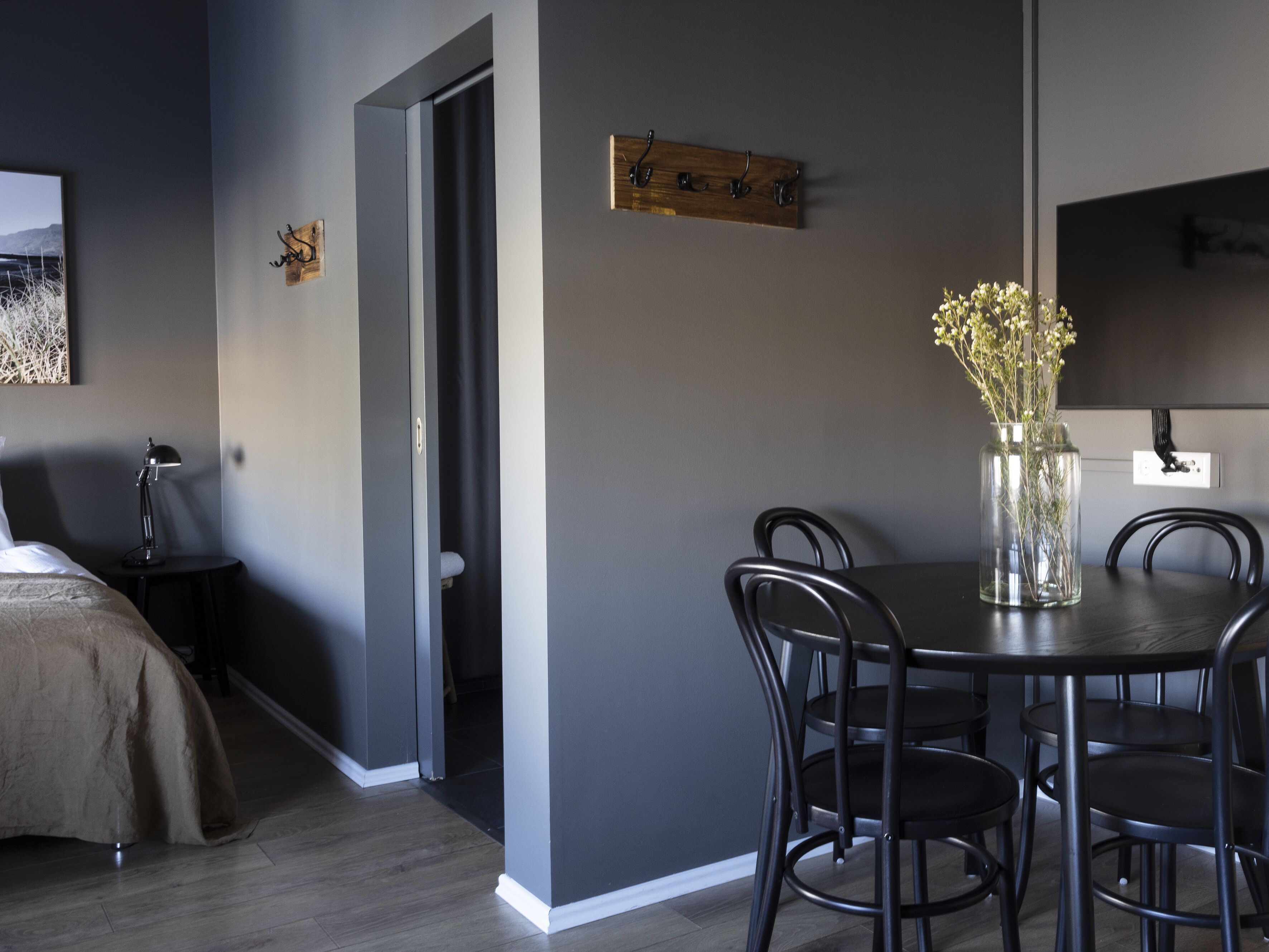 A modern dining area with a round table and chairs, a vase with flowers, and a coat rack on the wall.