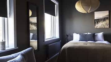 Ein Schlafzimmer mit großem Fenster, einem Bett mit weißen und dunklen Kissen, einem Nachttisch und einer Hängeleuchte.