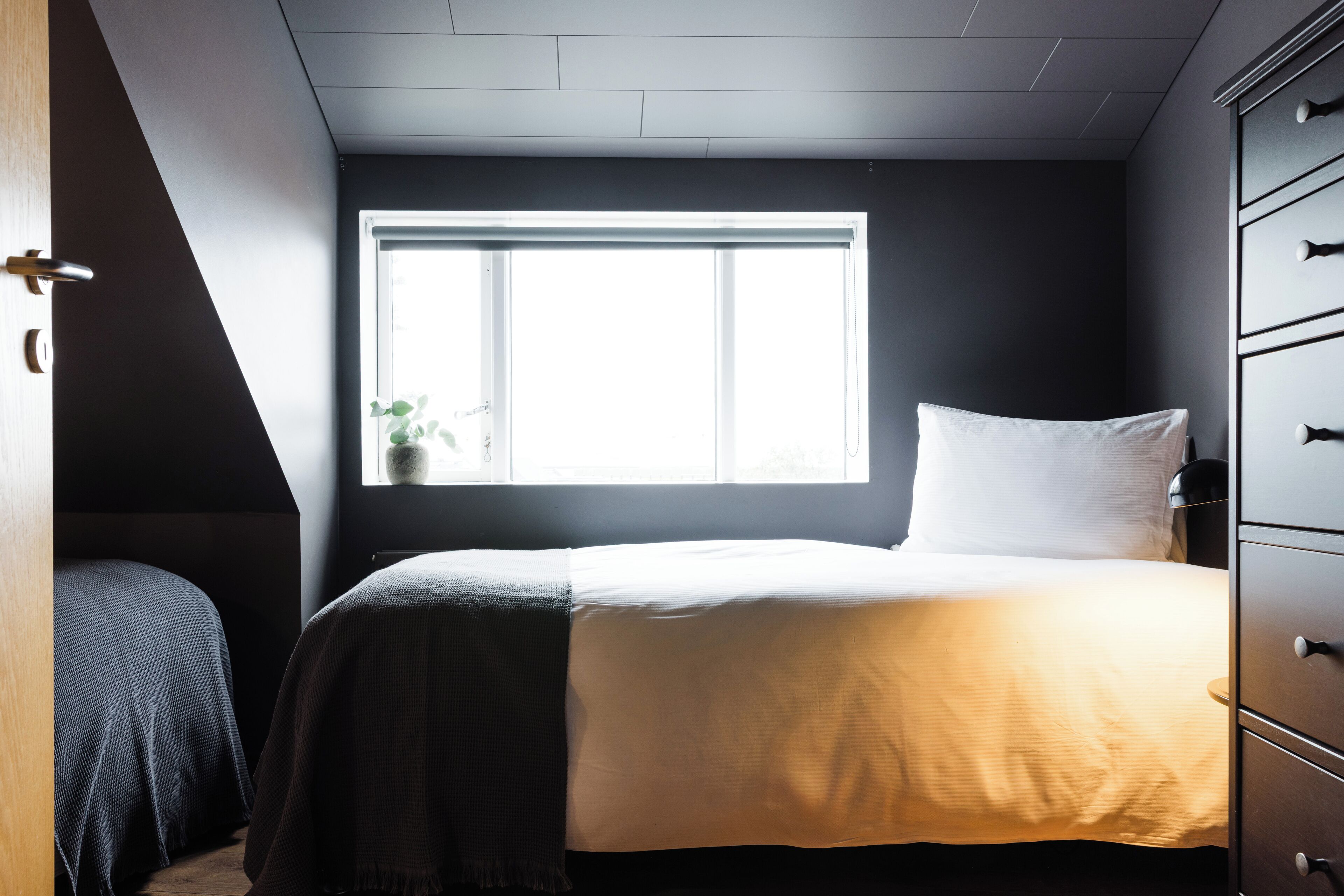 Een slaapkamer met een bed, een raam en een dressoir.