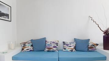 A modern room with a blue sofa set against a white wall, featuring patterned cushions and a clear glass candle holder.
