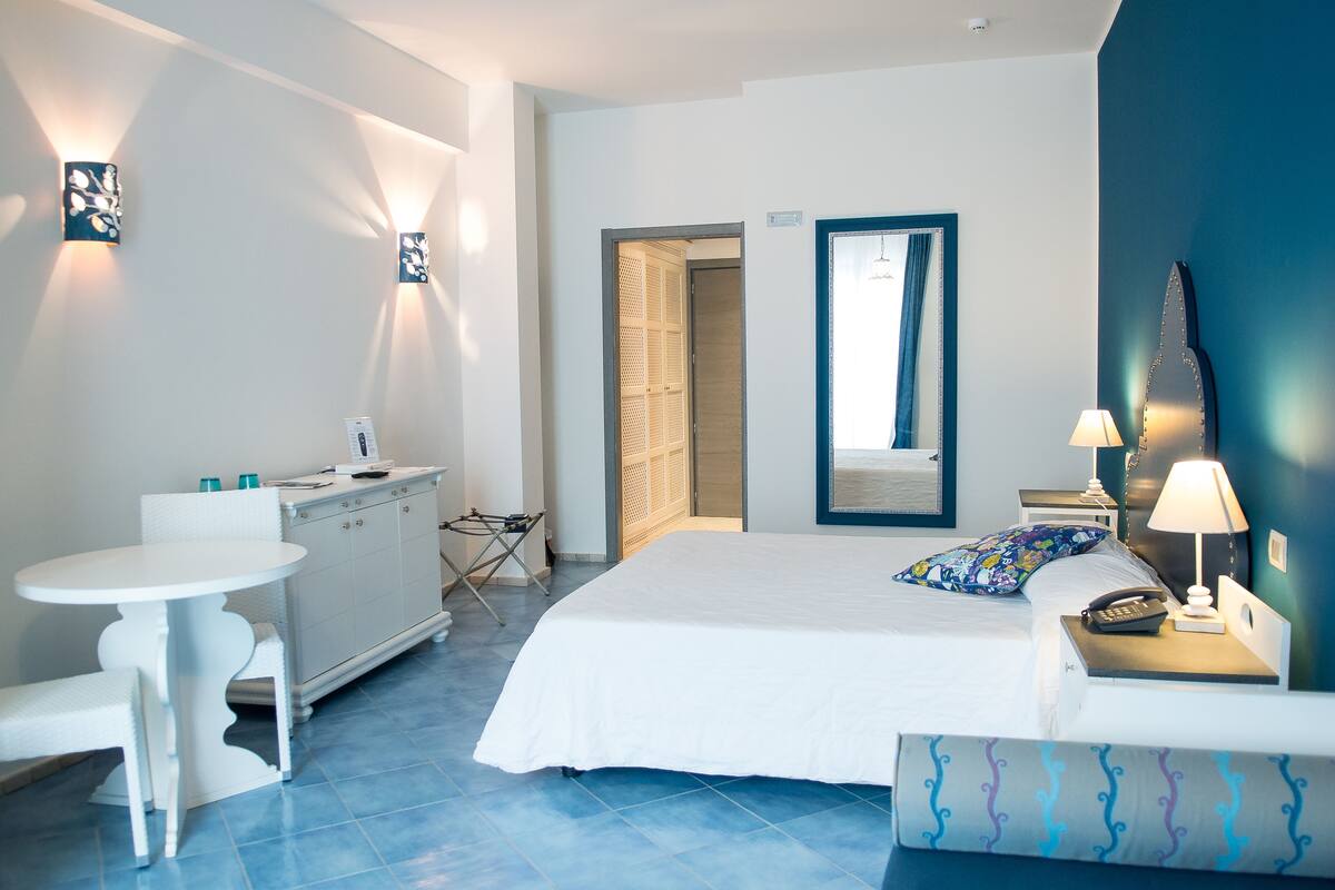A hotel room with a bed, bedside table, lamp, desk, chair, and a small table with a chair.