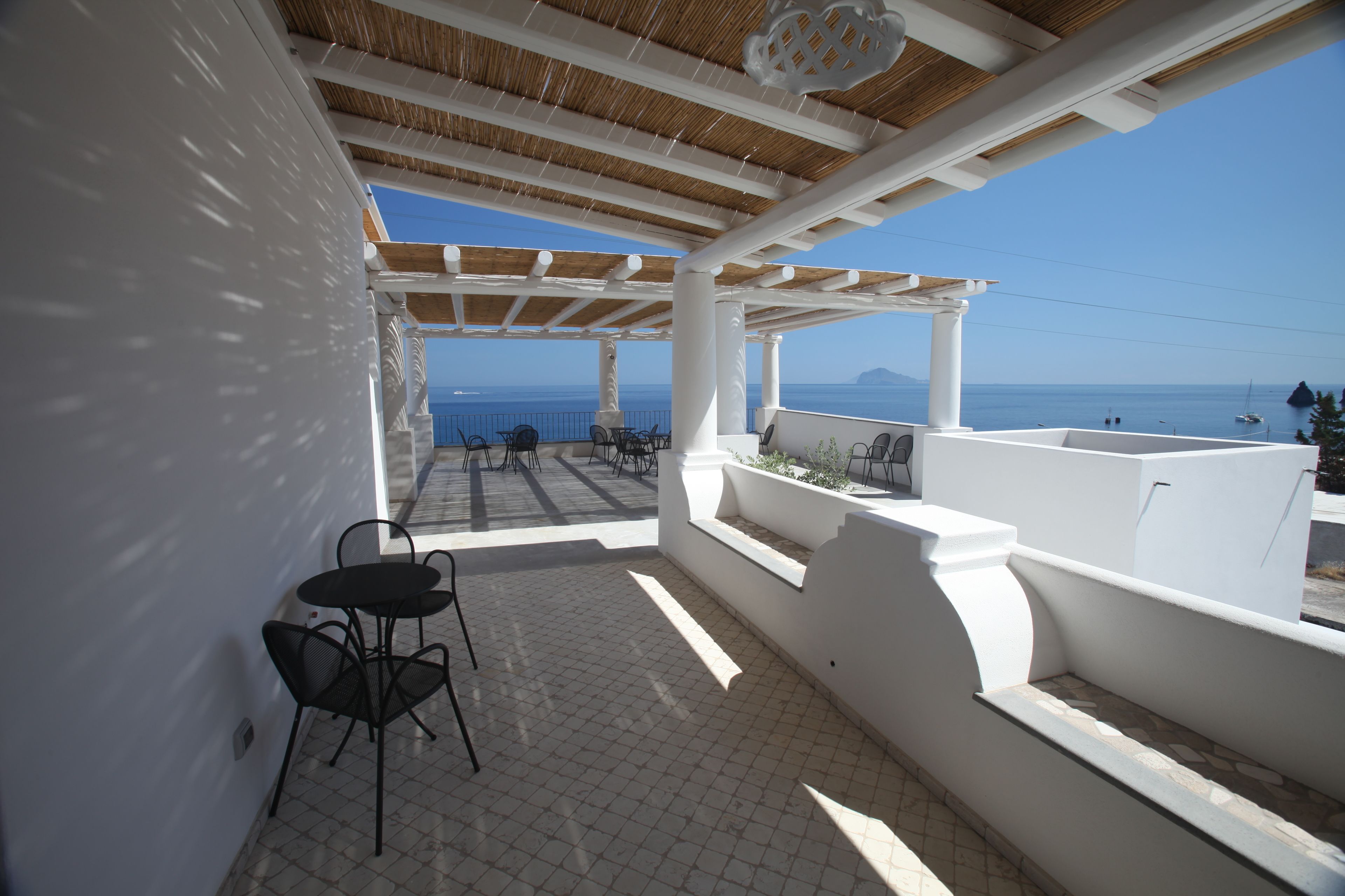 Une terrasse couverte avec vue sur la mer, comprenant une table et des chaises, des murs blancs et une pergola.