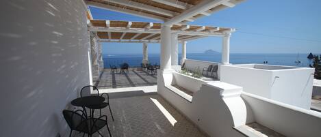 Une terrasse couverte avec vue sur la mer, comprenant une table et des chaises, des murs blancs et une pergola.