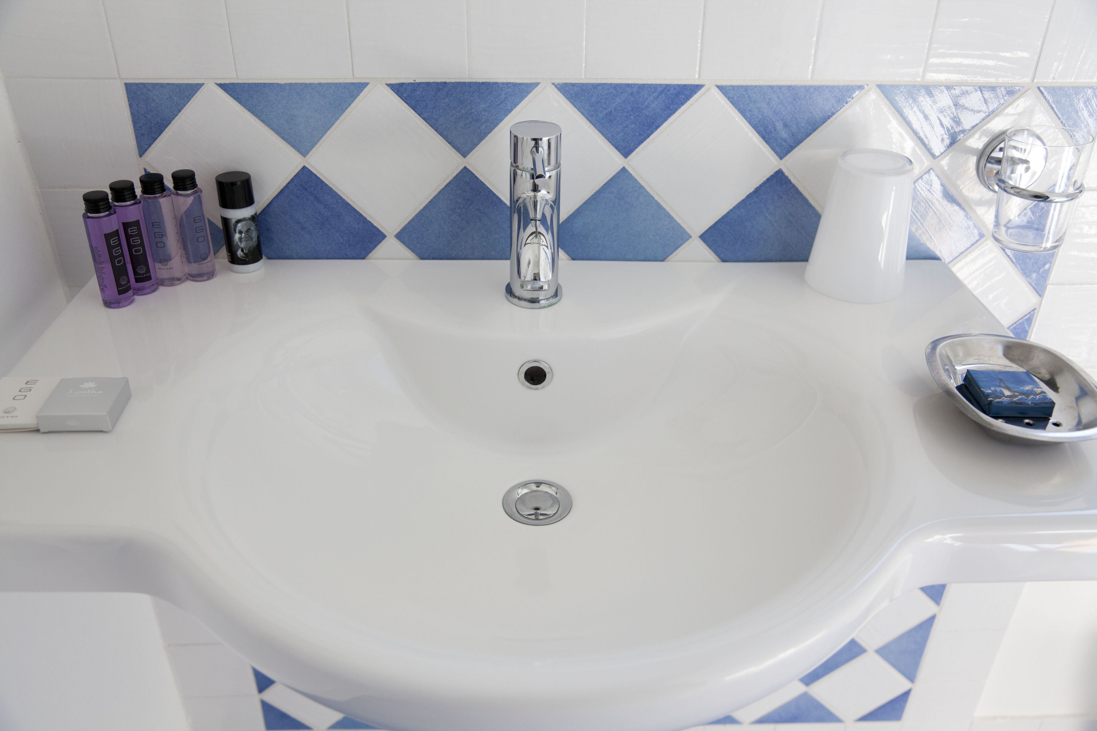 A bathroom sink with a chrome faucet, a white soap dispenser, and a blue and white tiled backsplash.